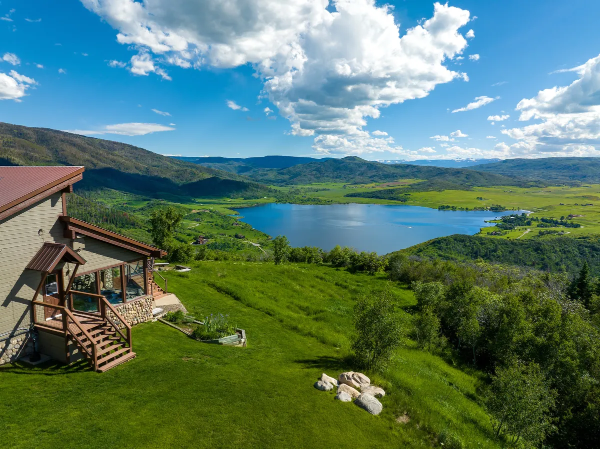 A wide view of the lodge, nestled beside a lake, with the surrounding green landscape and mountains providing a picturesque backdrop. The image suggests access to nature, hiking, fishing, picnicking, and family exploration all within the property’s proximity.