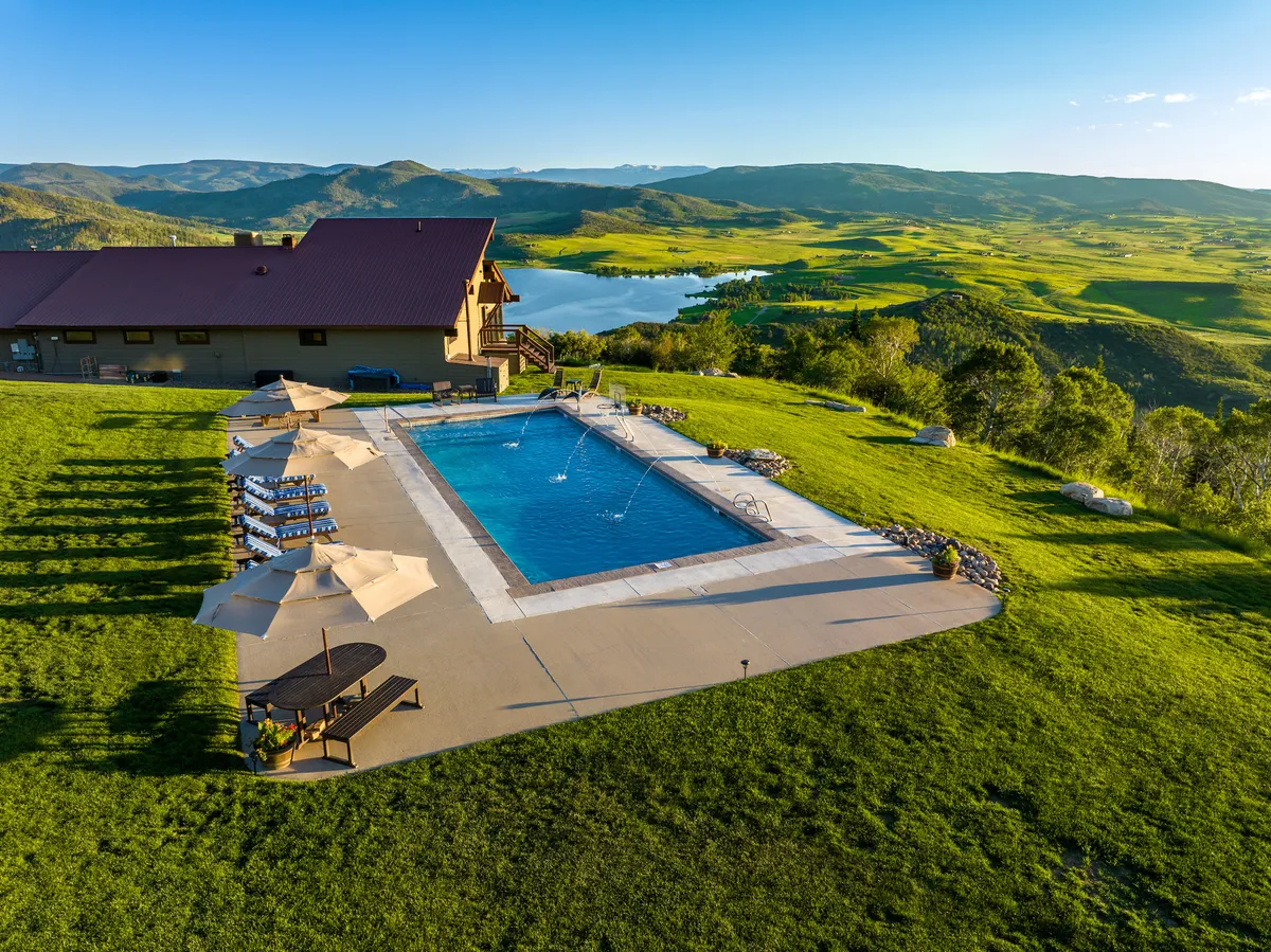An exterior view featuring a swimming pool overlooking a stunning mountain landscape, a manicured lawn, and ample patio seating. The setting is ideal for both informal team bonding and enjoying the tranquility of the mountains together.