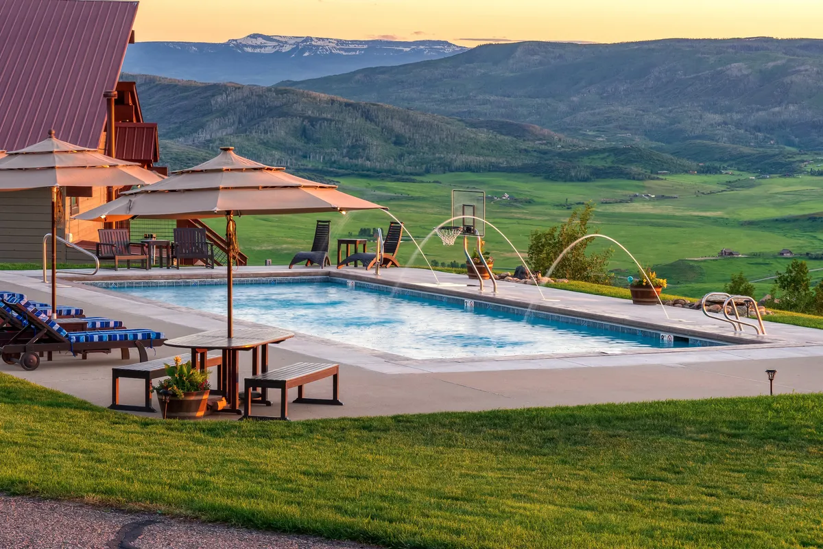 A tranquil summer scene featuring the estate’s private swimming pool, with outdoor seating and umbrellas set against a backdrop of mountains. The space invites sunbathing, swimming, and group relaxation, embodying the exclusive summer amenities mentioned in the section.