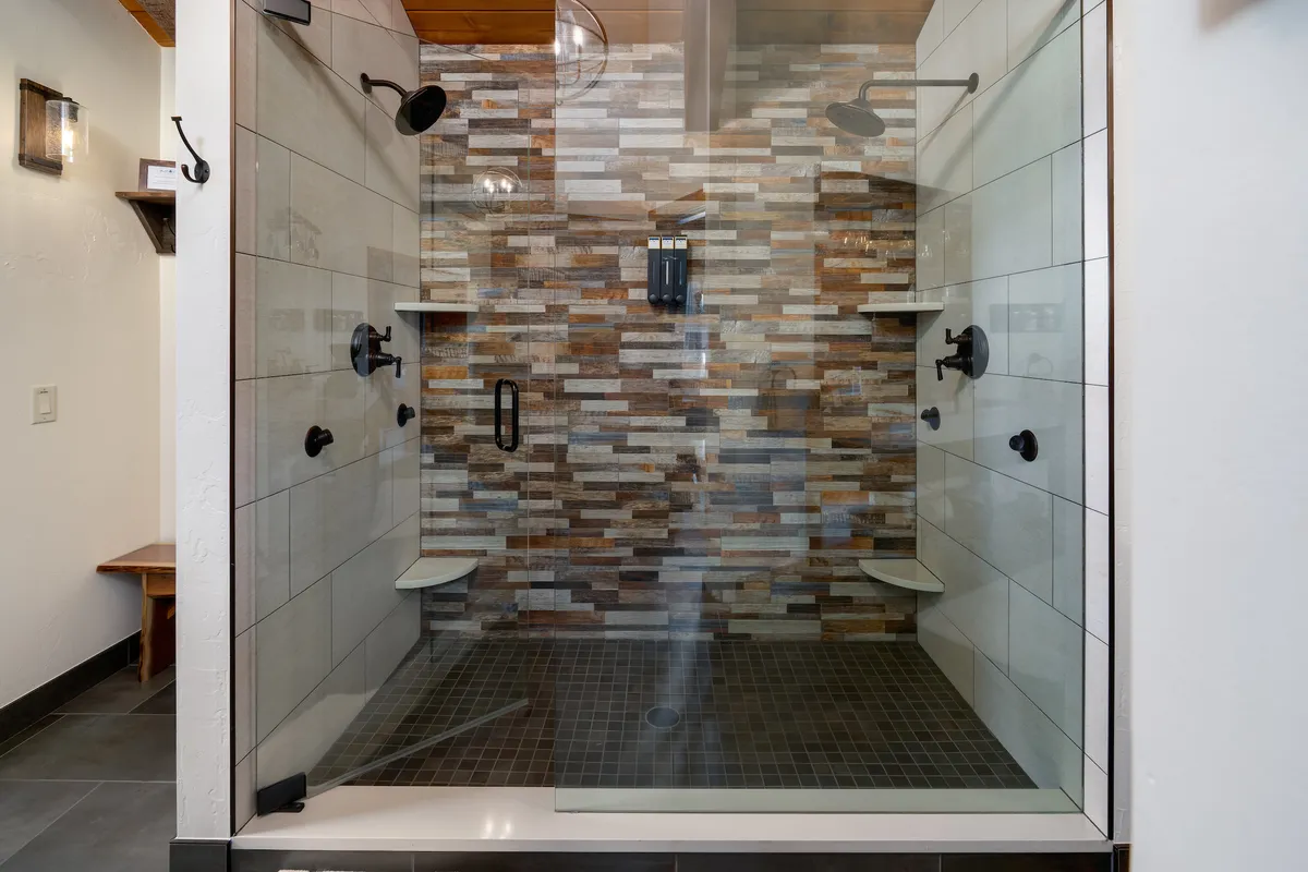 A modern bathroom featuring a spacious glass shower enclosure, textured stone wall, and sleek black fixtures. The ample space and contemporary style suggest both relaxation and functionality.