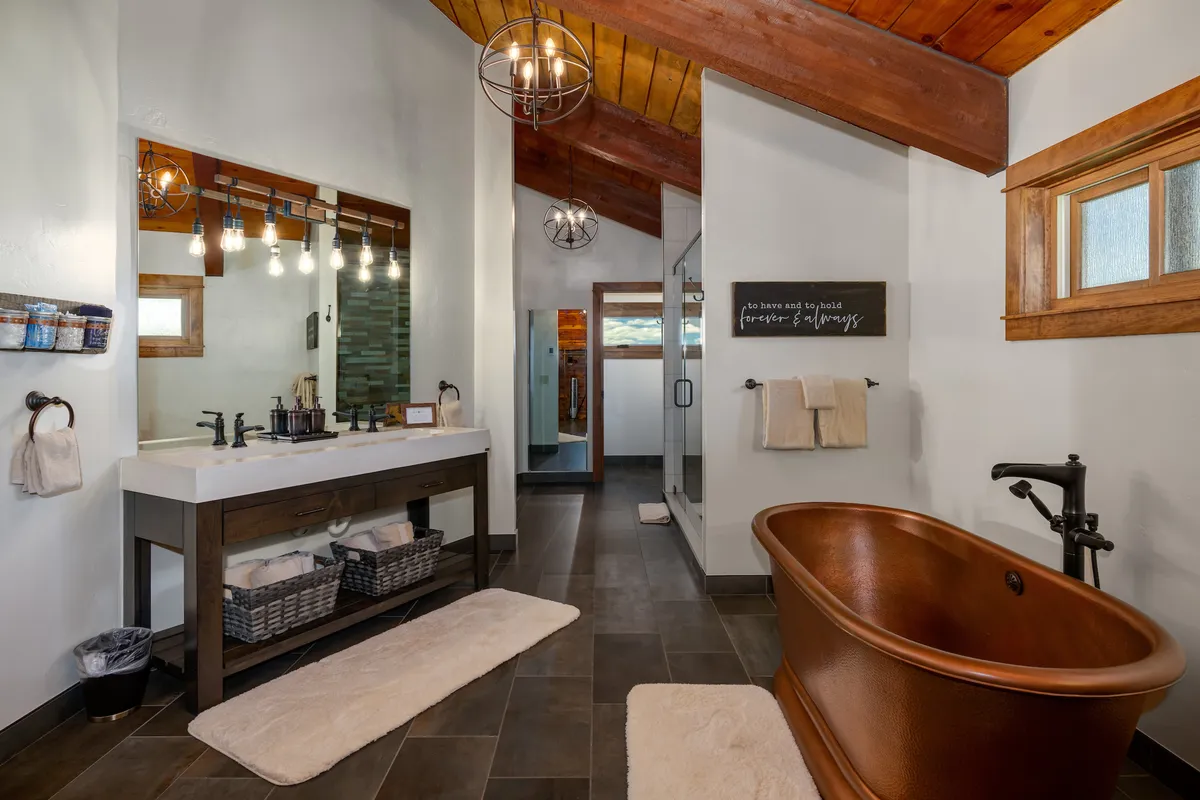 A luxurious bathroom with a freestanding copper bathtub, double vanity, large mirror, and elegant hanging light fixtures. The space feels both tranquil and indulgent, perfect for winding down after a day of adventure.