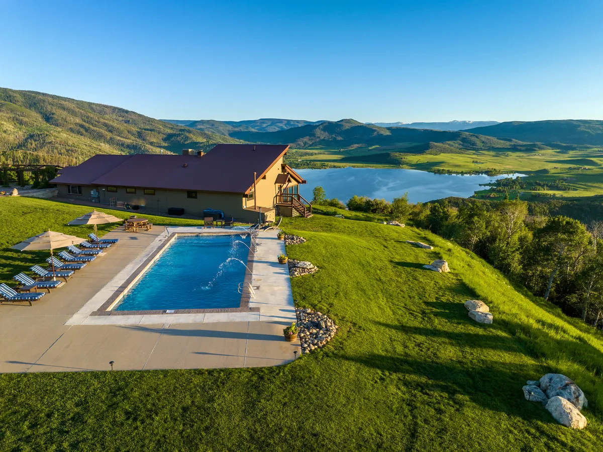 Featuring a sparkling swimming pool set against a backdrop of lush lawn, mountain vistas, and a shimmering lake, this image encapsulates the estate’s sense of privacy and relaxation. The pool area is inviting for swimming, sunbathing, or simply soaking in the view.