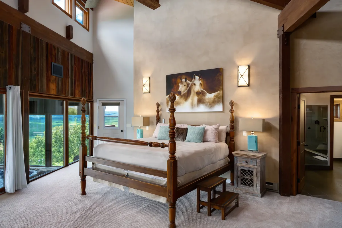 A serene bedroom featuring a four-poster bed placed next to large windows that overlook a stunning landscape. The room is adorned with horse artwork and flooded with natural light, creating a tranquil retreat ideal for relaxation.